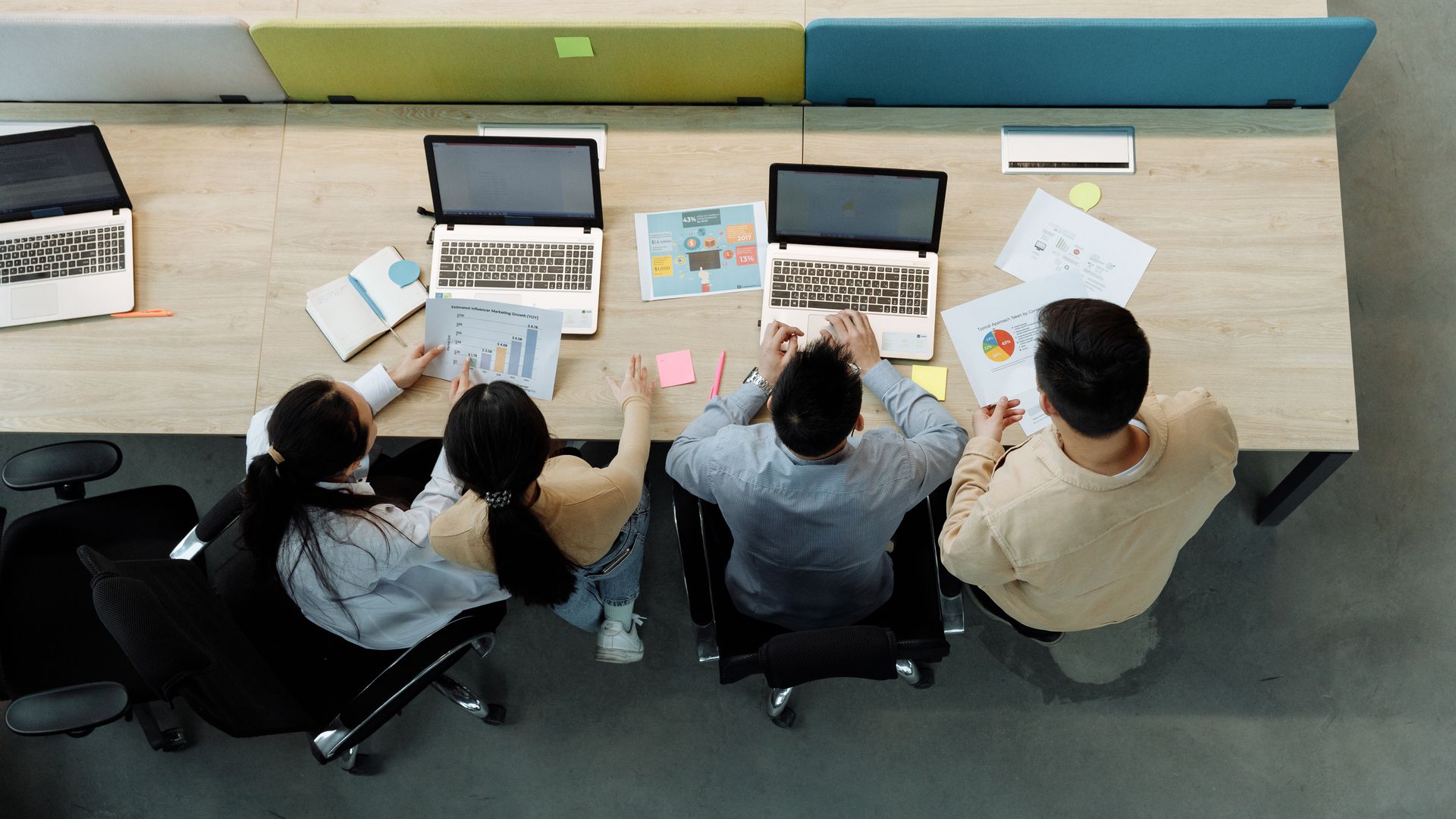 Vue aérienne de quatre collègues travaillant sur des ordinateurs portables et des documents à un bureau partagé.